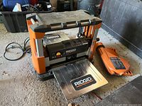 Front left angle view of planer with infeed table attached and plastic guard beside on concrete floor