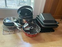 Overview of multiple pots, pans, and bakeware items stacked together including bundt pans, cake pans, and racks.
