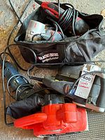Power sanding tools inside a Black & Decker ProjectMate carrying bag, including corded sanders with red and black coloring, cords visible.