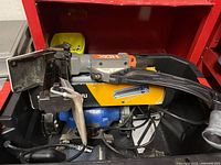 Photo showing HDX brand flooring nailer resting on a box and a visible portion of the blue 6-inch bench grinder underneath