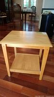 Side view of a wooden side table placed on a hardwood floor, showing the rectangular top and lower shelf with visible marks.
