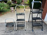 Three step ladders shown side by side outdoors: one small one-step ladder, one medium (3ft) two-step Gorilla ladder with handlebars, and one tallest Gorilla ladder model GLS 3HDC with three steps.