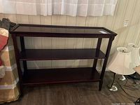 Full view of the three-tiered dark wooden side table placed against a wall, showing its rectangular shape and structure.