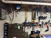 Basement workbench showing brown metal toolbox under wall-mounted hand tools and blue plastic bins