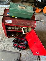 Red metal tool chest on wheels with green metal toolbox on top and red/black tool bag on floor beside it, showing overall contents and condition