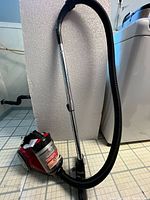 Photo showing full vacuum cleaner with taped handle, hose, metal wand and floor attachment.