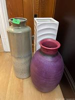 Three vases: purple round vase with red rim, tall gray cylindrical vase, tall white square vase with wave pattern.