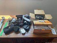 Overview of vintage cameras, camera accessories, tripods and boxes on wooden surface.