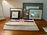 Photo showing four framed prints and a folded WWI/RCAF banner/poster on a table