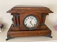 Front view of the wooden antique mantle clock showing wood and metal decorative accents and feet
