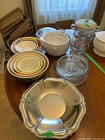 Full lot on table showing nested Pyrex mixing bowls, glass measuring cups, glass baking dishes, white Betty Crocker mixing bowl, and silver serving platter.
