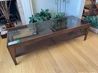Front angle view of wood coffee table highlighting smoked glass top panels and woven cane lower tier.