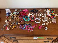 Wide view of the costume jewelry laid out on a wooden surface showing multiple necklaces, bracelets, earrings, brooches, and pins.