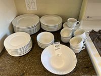 Full set of white ribbed design plates, bowls, cups and saucers on a kitchen counter