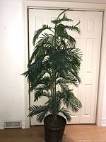 Full view of 6-foot tall artificial palm plant standing near closed closet doors, showing full height and lush fronds in dark woven basket pot.