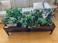 Eight artificial plant sets on a coffee table varying in size and container material.