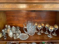 Wider view showing two glass beer steins centrally placed, salt and pepper shakers grouped on left, six decorative glasses with gold rim on right
