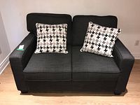 Front view of the dark gray fabric love seat showing two patterned throw pillows