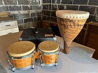 Wide view of two small Afro-Cuban drums and one wooden drum with skin head, including soft carrying case