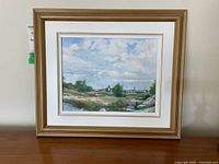 Framed oil painting showing the full artwork and frame, portraying a landscape with water, green land, and sky with clouds.