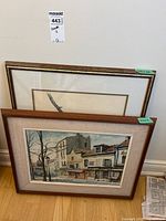 Two framed prints leaning against a wall, identified as street scene print with linen matte and bird print in wood frames.