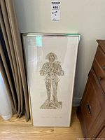 Full view of single framed brass rubbing with medieval male figure in armor holding small dog, upright against wall.