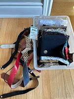 Photo showing a white bin filled with vintage purses including black fabric purse, floral tapestry purse, and assorted belts to the left of the bin in various colors