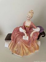 Front angled view of Royal Doulton figurine 'Reverie' showing seated woman in pink gown holding book