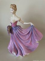 Front and left angle of Royal Doulton 'Rachel' figurine showing detailed pink and purple dress, delicate facial features, and fan accessory.