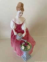 Front view of the Royal Doulton Alexandra figurine showing the woman watering flowers in a pink dress.