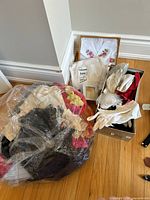 Photo showing a large plastic bag with assorted scarves and a box with white and beige gloves plus a framed embroidered handkerchief.