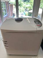 Top and front view of Panasonic SD-YD200 bread maker showing white body and digital control panel with buttons.