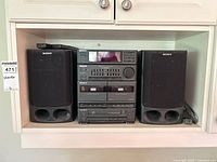 Front view of Sony FH-B5CD stereo system with two speakers on each side placed on a shelf; includes remotes on top