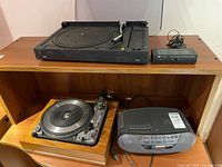 Three audio devices on and inside a wooden shelving unit: Dual 1019 turntable, Braun PS 550 turntable, Sony CD radio cassette player, and JEC TC-778 phono equalizer with adapter, showing overall lot contents