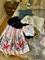 Photo of vintage ladies' clothing set on bed including sweaters, cotton skirt, and slips/trouser liners.
