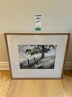 Framed watercolour landscape painting showing tree, fence, hill and misty background against wall.
