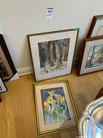 Two framed watercolour paintings leaning against a wall: one floral with orange-yellow tulips in a gilded frame, the other a winter woodland scene in a wood frame.