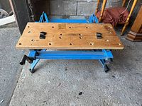 Photo showing front view of the Black & Decker work table with wooden top and blue metal frame on concrete floor.