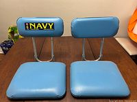 Front view of two blue stadium chairs showing padded seats and backrests, one with NAVY sticker