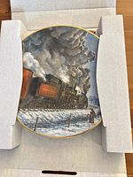 Plate in shipping insert, showing locomotive scene and box packaging