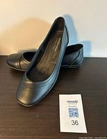 Side and angled view of both black flats showing uppers and branding on insole