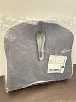 Front of sealed charcoal cushion in plastic wrap showing coccyx cut-out and barcode label