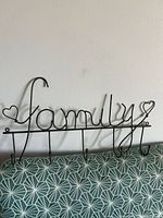 Front view of black metal “family” wall hook rack showing cursive lettering, heart accents, five hooks