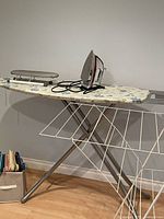 Overview of ironing board set up with iron, sleeve board, drying rack, bin of hangers