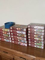 Nineteen Cobble Hill Easy Handling puzzle boxes stacked on cabinet