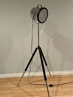 Front view of tripod floor lamp, spotlight head, cord visible