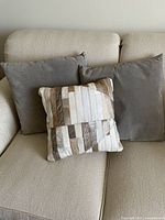 Two grey suede pillows and one patchwork hide pillow on sofa