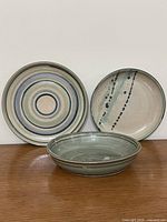 Three studio pottery pieces (two plates, one bowl) on wood surface