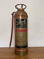 Front view of vintage Pyrene copper and brass fire extinguisher with label and hose visible