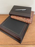 Closed journals stacked on writing box with pen on top